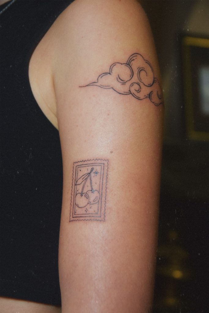 Tattoos sur un bras : nuages en haut et un timbre en bas.