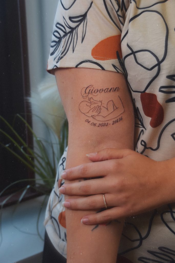 Tatouage sur un bras représentant un texte qui entoure un mère allaitante. 