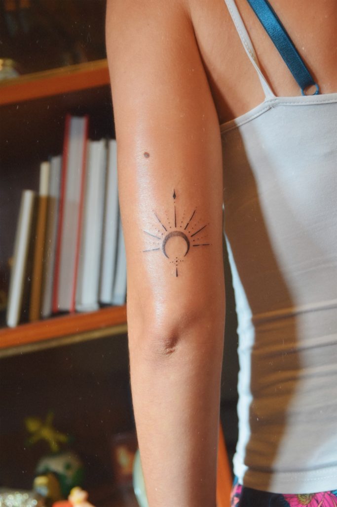 Tatouage représentant un soleil stylisé sur le bras d'une personne.