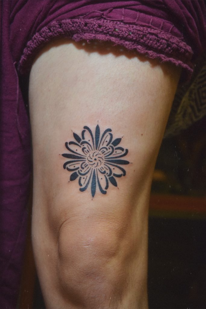 Tatouage floral détaillé sur un genou, avec des pétales et un centre orné.