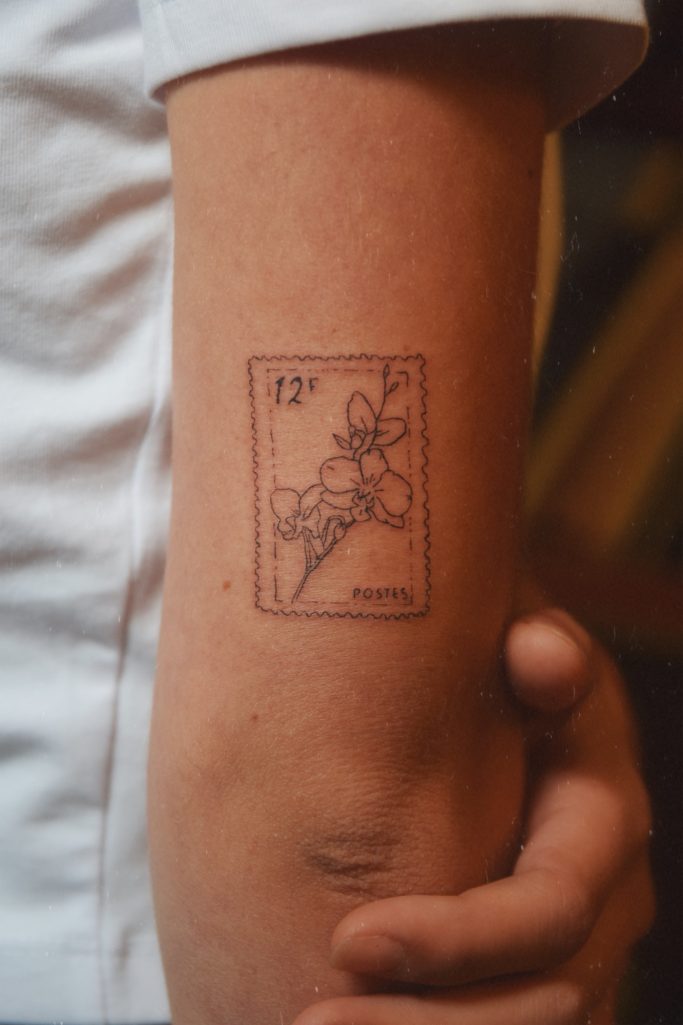 Tatouage de timbre avec une fleur sur le bras d'une personne.