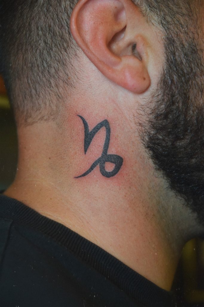Tatouage du signe astrologique du Capricorne sur la nuque d'un homme.