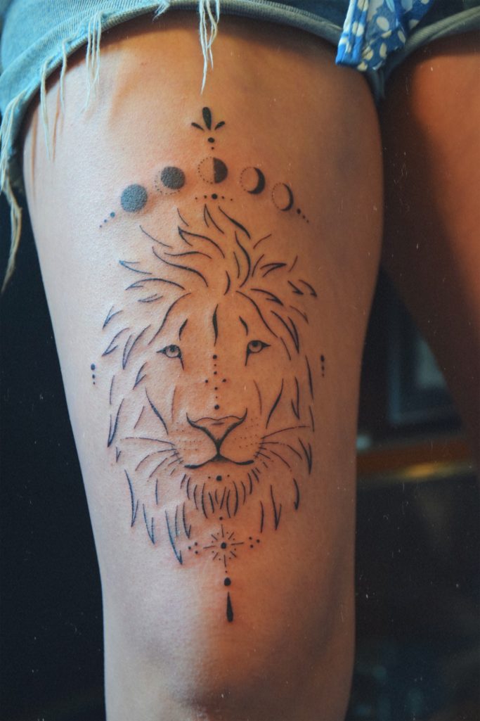 Tatouage d'un lion stylisé avec des phases lunaires sur la cuisse.