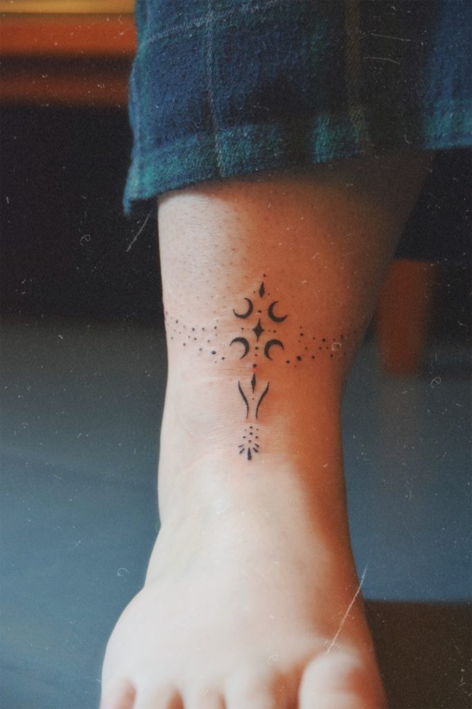 Tatouage délicat sur la cheville avec motifs de lune et ornement.