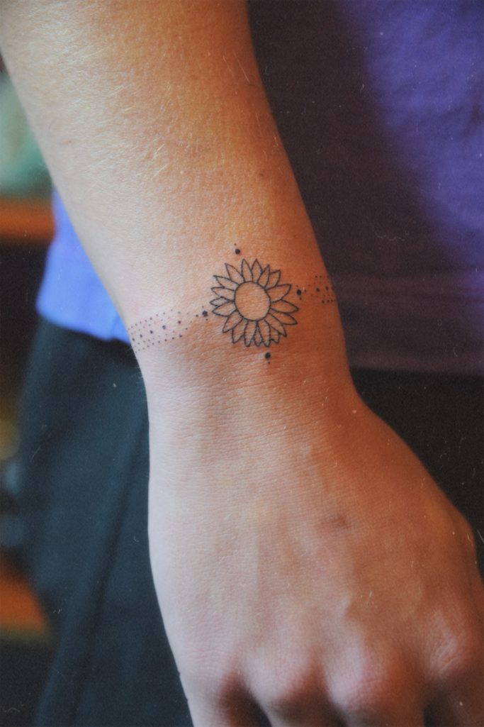 Tatouage délicat en forme de tournesol sur le poignet d'une personne.