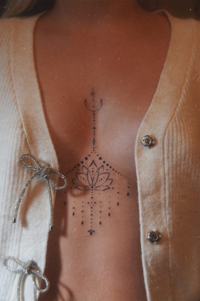 Tatouage underboob ornemental avec un otus, porté sous un cardigan beige.