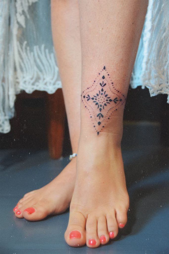 Tatouage géométrique noir sur la cheville, orné de petits points.