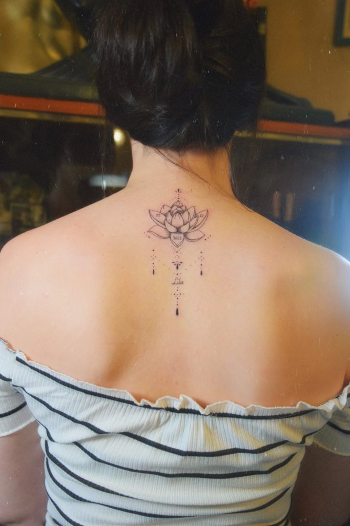 Tatouage d'un lotus délicat en haut du dos, avec des motifs ornementaux suspendus.